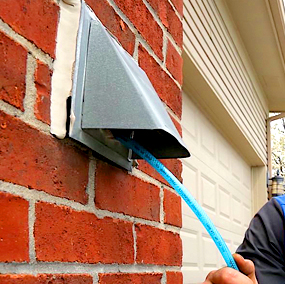 A PowerVac technician inserts a cleaning hose into a dyer vent during dryer vent cleaning.